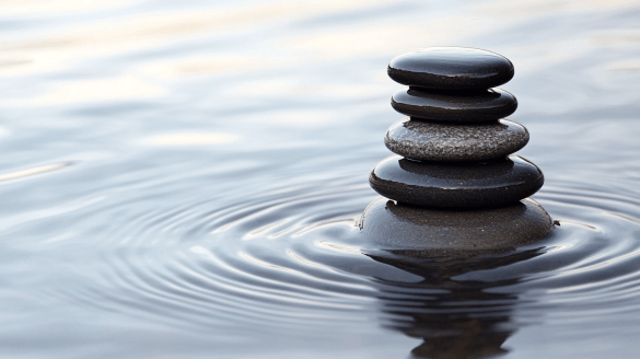 A serene arrangement of black stones stacked on top of each other, creating a balanced structure in calm water, symbolizing tranquility.